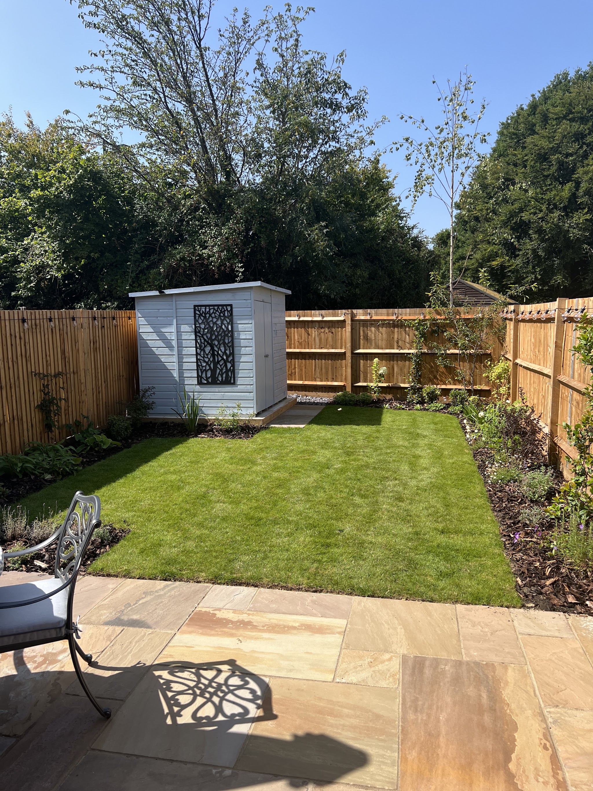 A finished new-build back garden with lawn, sandstone patio, shed and planted borders
