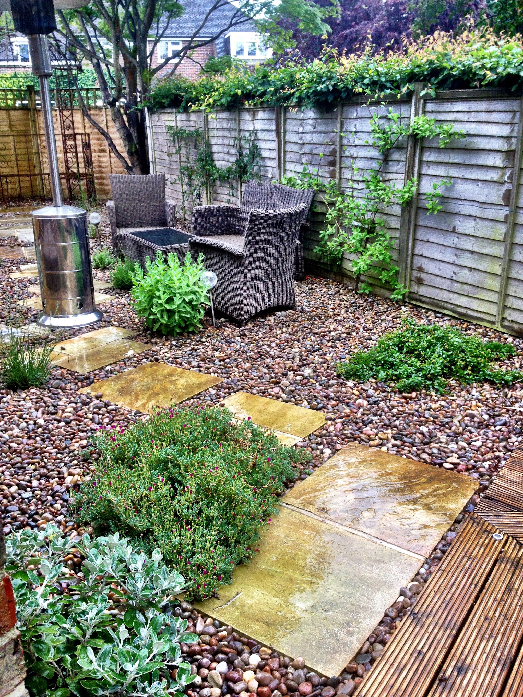A gravel garden with stepping slabs, rattan seating and climbers on the fence