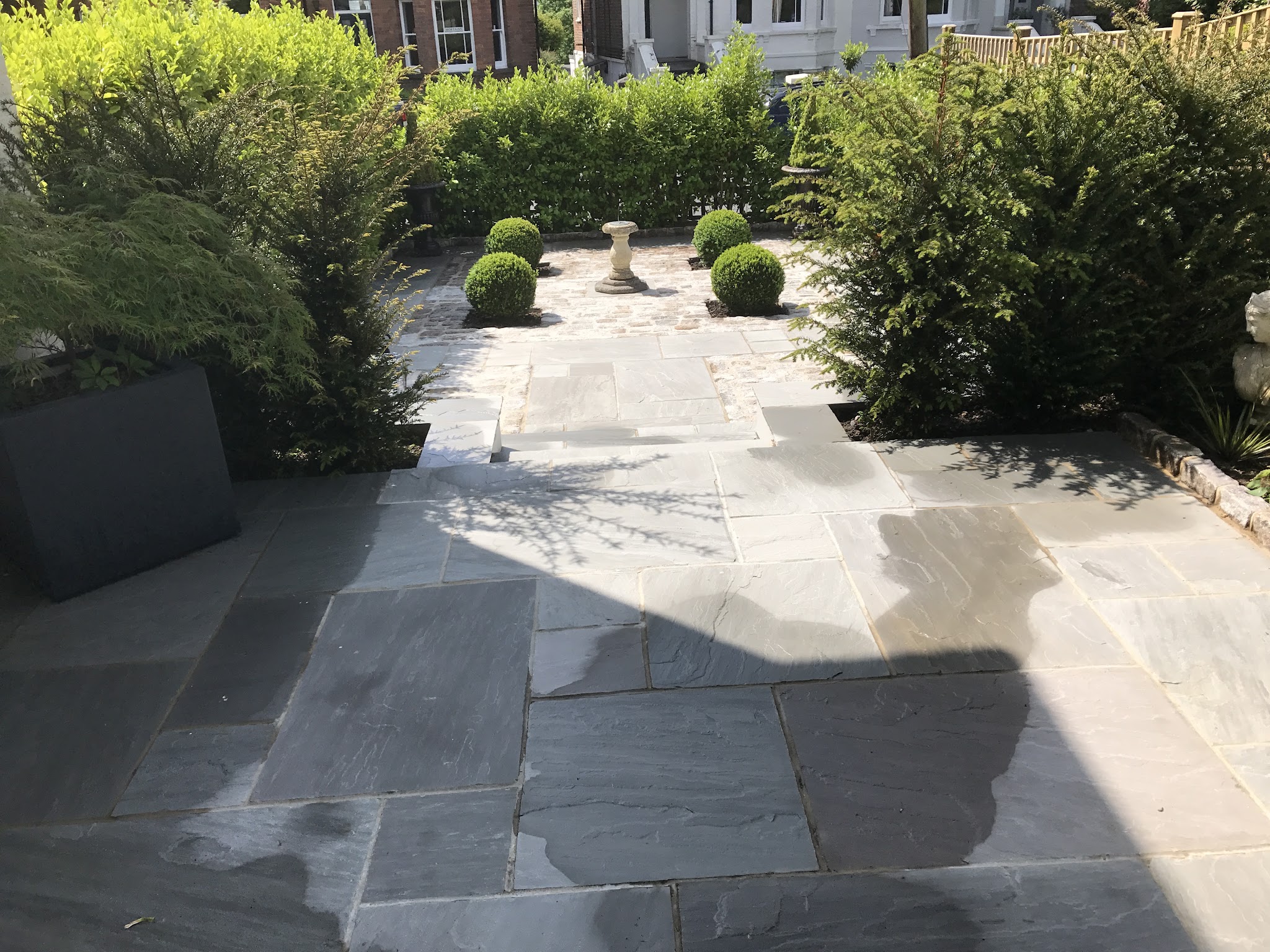 A grey stone terrace with box balls and a sundial