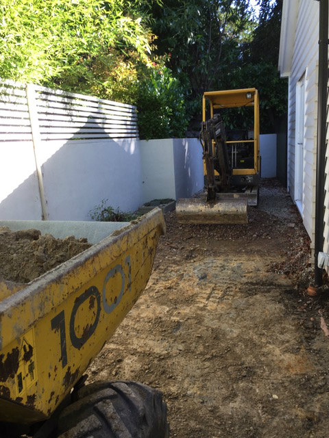 A mini digger clearing ground in a narrow side garden
